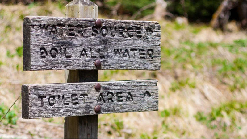 Wooden signs for toilets and a water source on a trail.