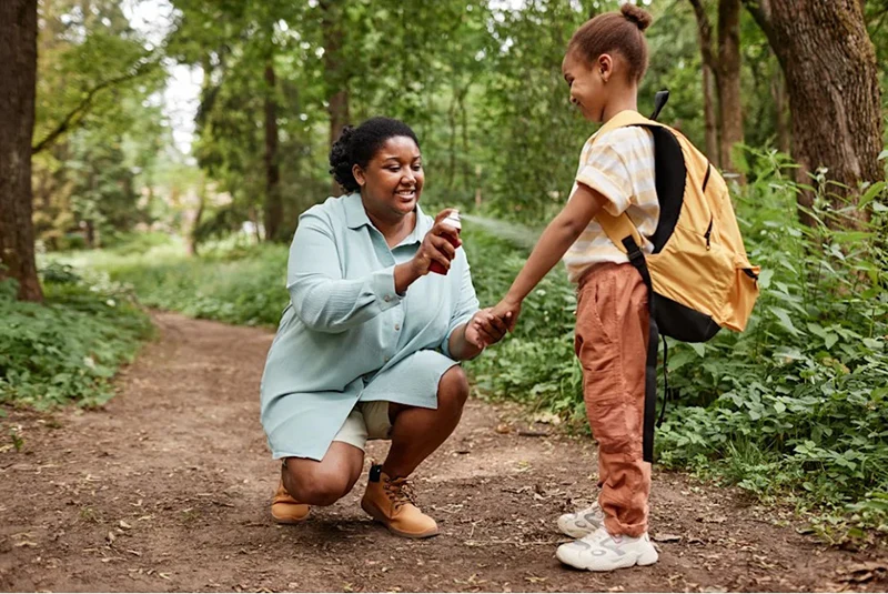 A lady spraying insect repellent on a child.