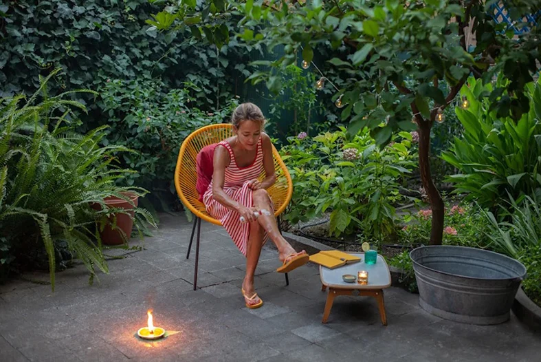 A lady spraying her leg while sitting in a chair.