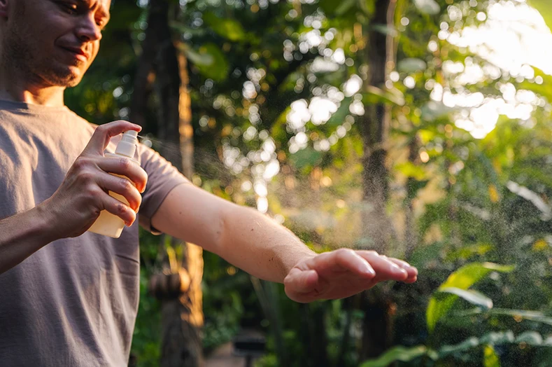 A person spraying insect repellent on their arm.