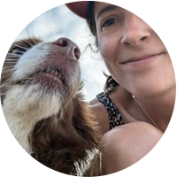 Close-up selfie of a smiling woman with short hair and a brown and white dog looking up.