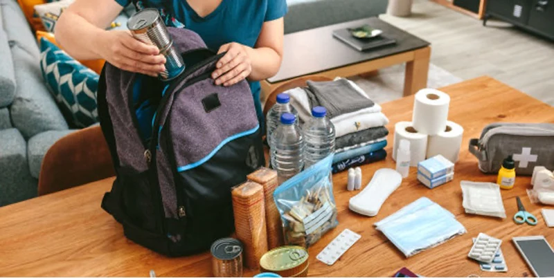 A person packing a backpack with emergency supplies.