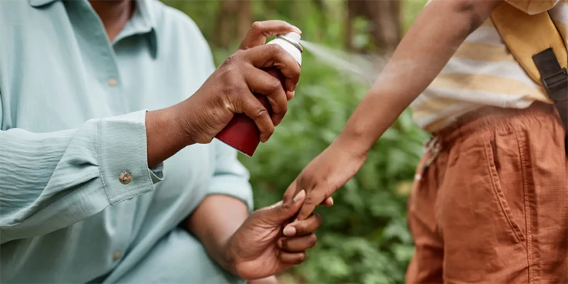 An adult spraying insect repellent on a child.