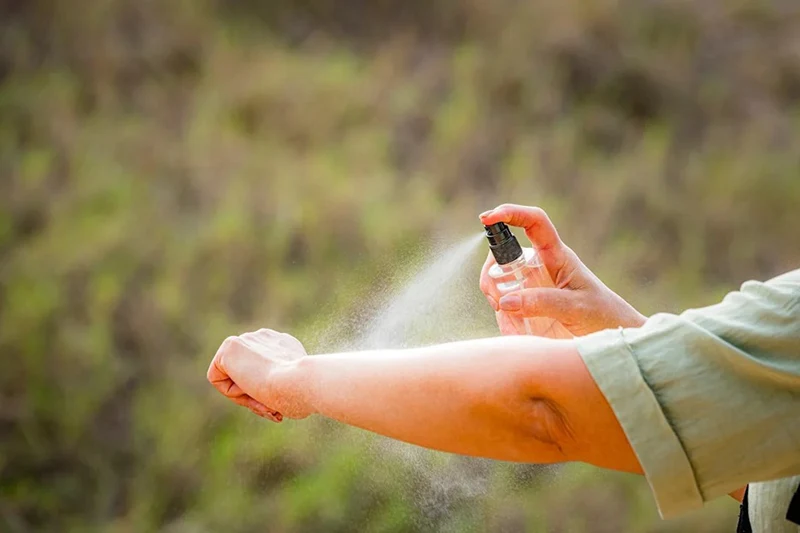A person spraying insect repellent on an arm.