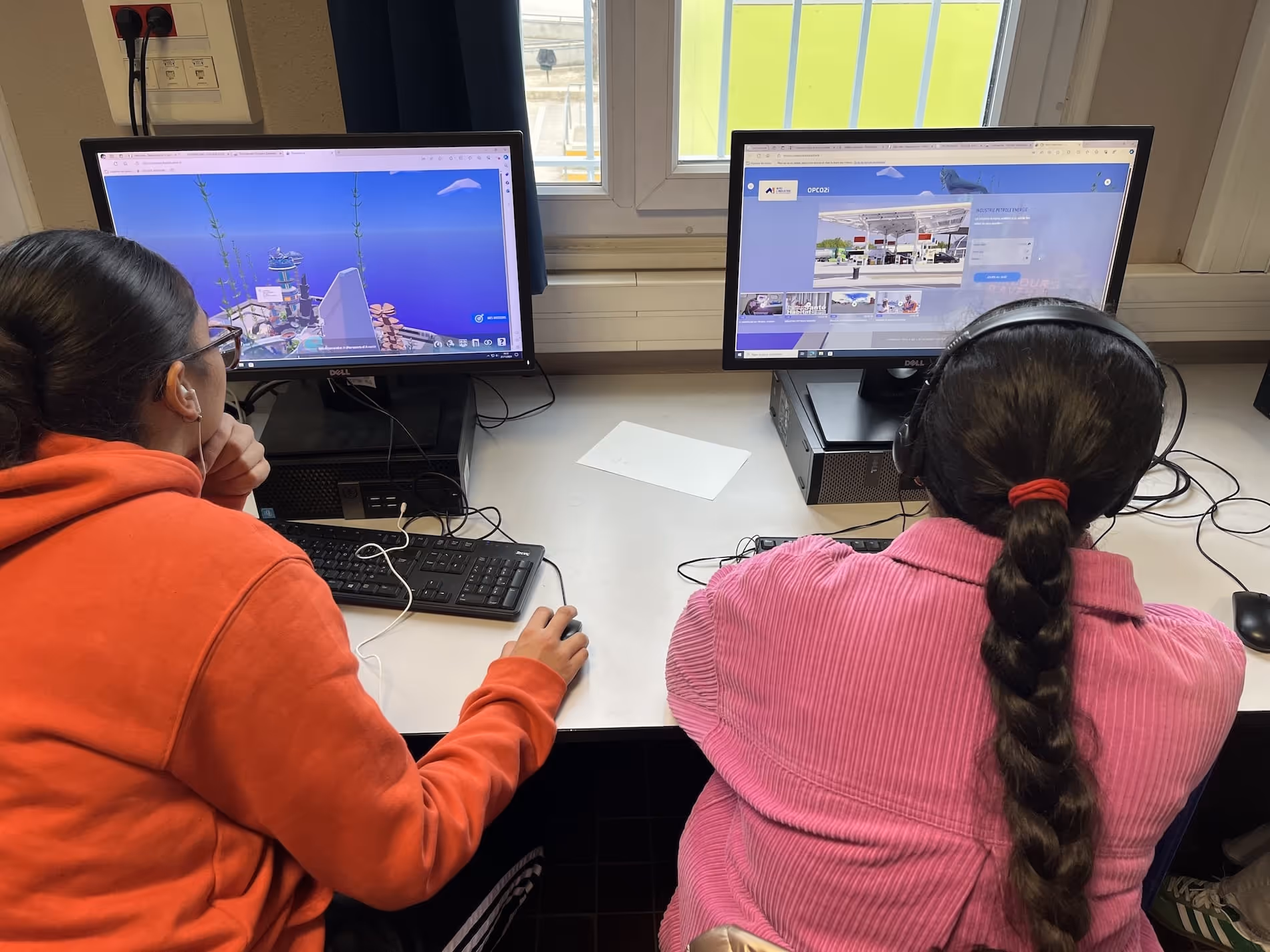 Two people sitting side by side at a desk using desktop computers with headphones.