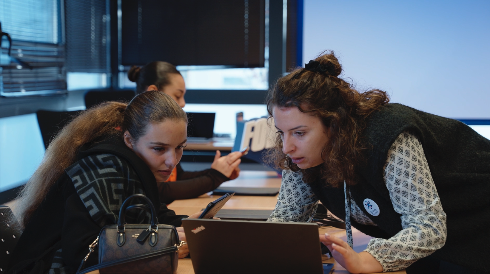 Office with several people working at desks with computers and wearing headsets, a woman standing and smiling.