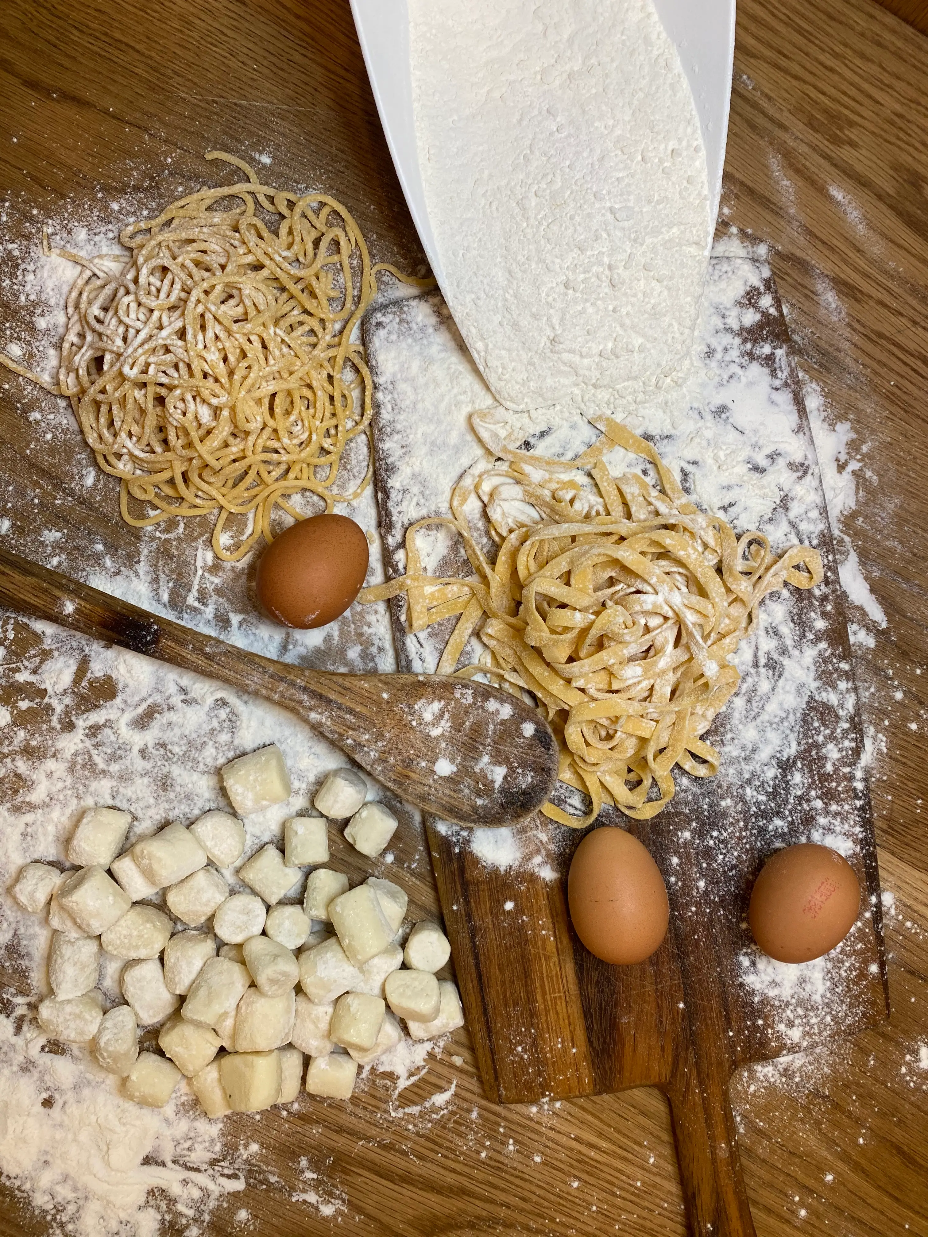 Fresh tagliatelle, potato gnocchi, eggs and flour on a wooden board