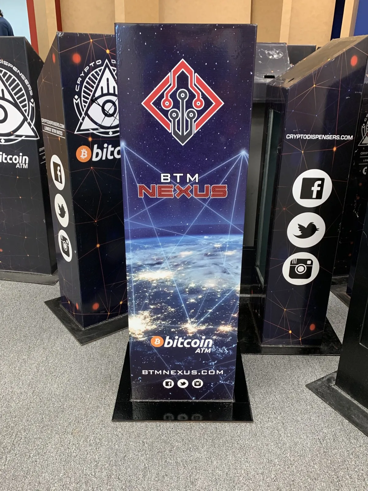 A BTM Nexus Bitcoin ATM cabinet surrounded by Crypto Dispensers-branded ATM cabinets.