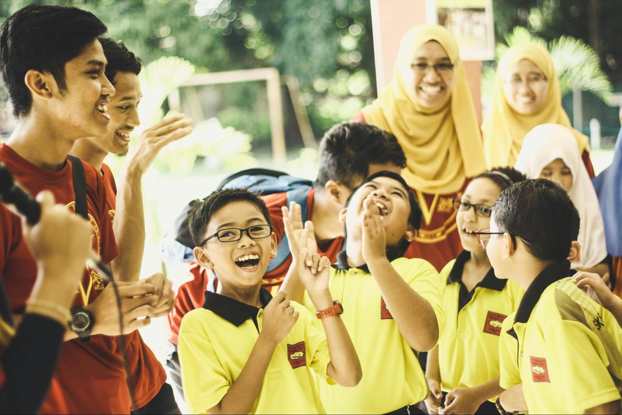 A cheerful group of students laughing and interacting with their teacher during an outdoor school activity, capturing a joyful learning moment.