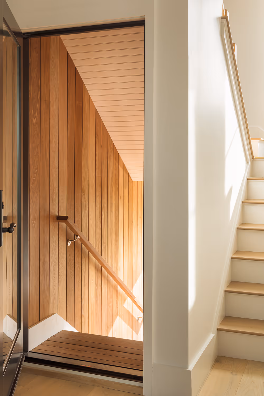 Wooden door with handrail, glass panel, and white staircase in modern interior