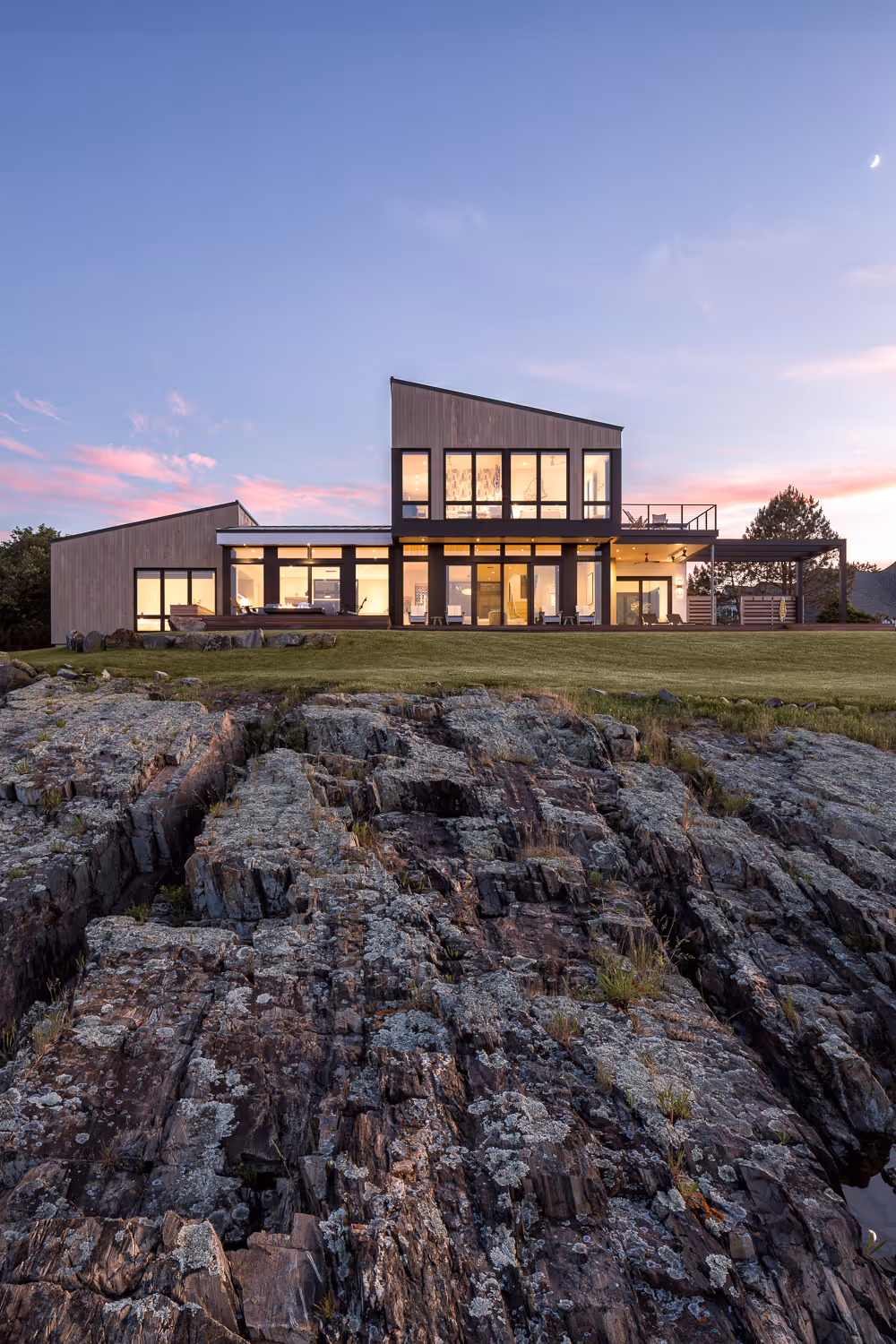 Modern house with large windows on rocky terrain at sunset