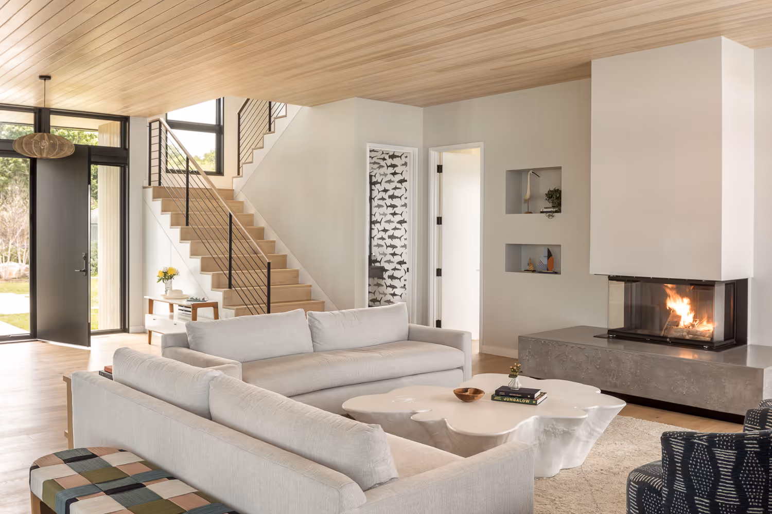 Modern living room with wooden stairs, fireplace, and large windows