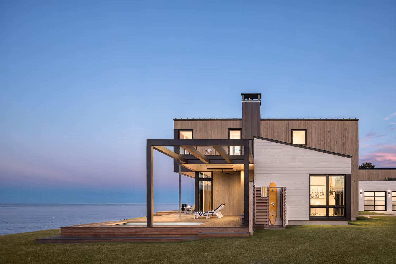 Modern beach house with deck, surfboard, and ocean view at sunset