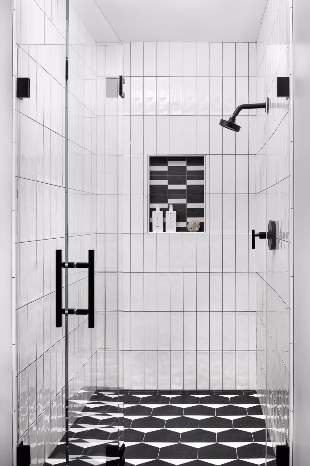 Modern glass shower with white tiles, black fixtures, and hexagonal floor