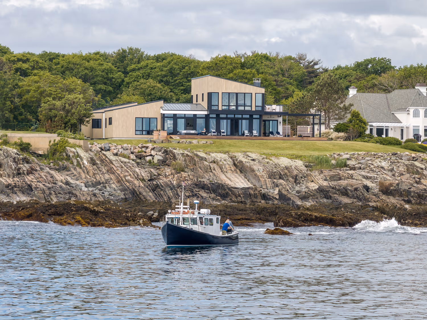 Boat near rocky coastline with modern glass house on grassy cliff