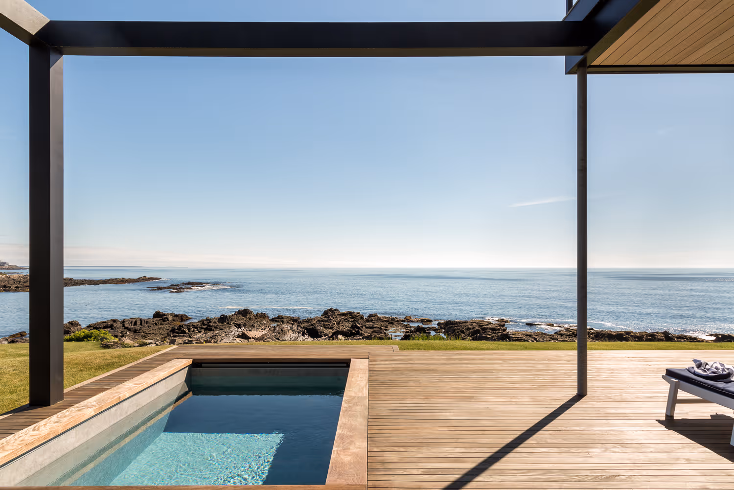 Modern pool overlooking rocky coastline with calm blue ocean horizon