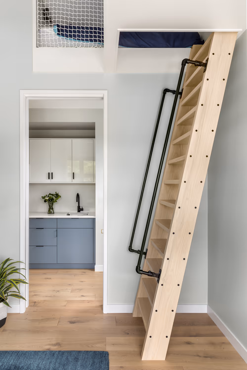 Wooden ladder leading to loft, with kitchen and blue rug in view