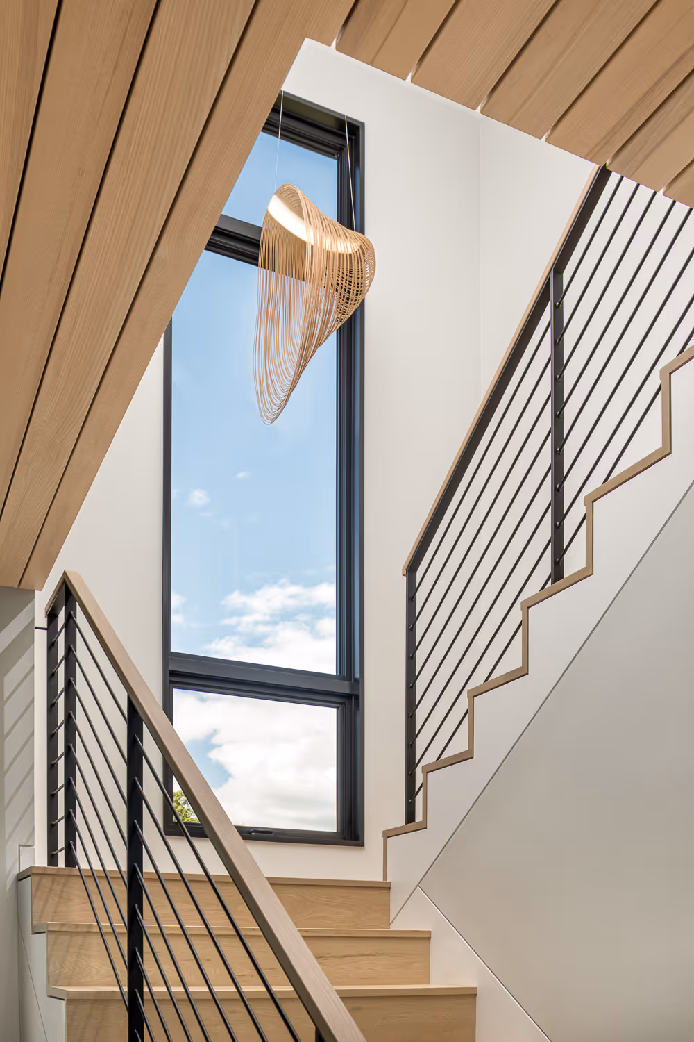 Modern staircase with wooden steps, sleek railing, and hanging sculptural light fixture