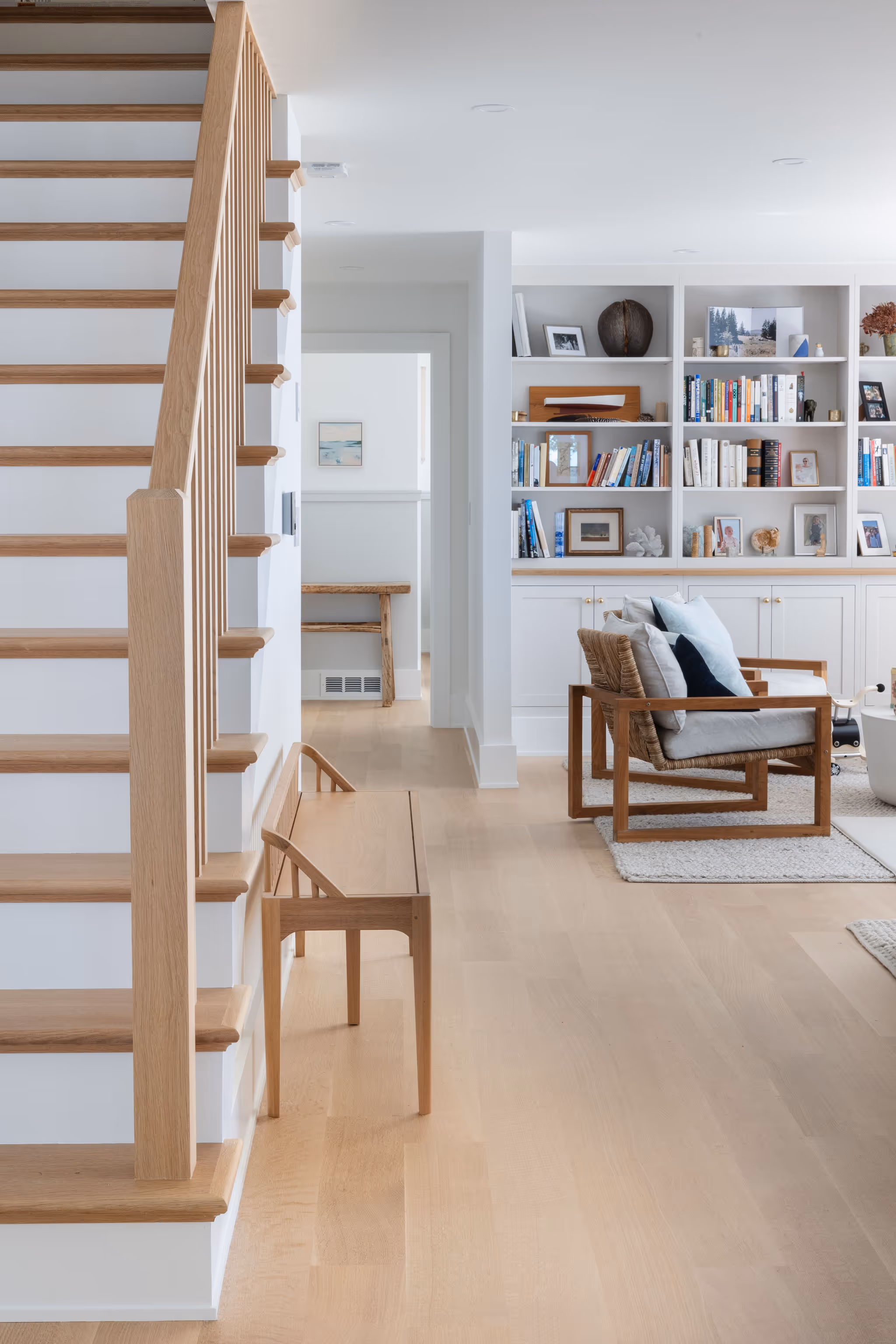 Minimalist interior with wooden stairs, bookshelf, and modern wooden chair