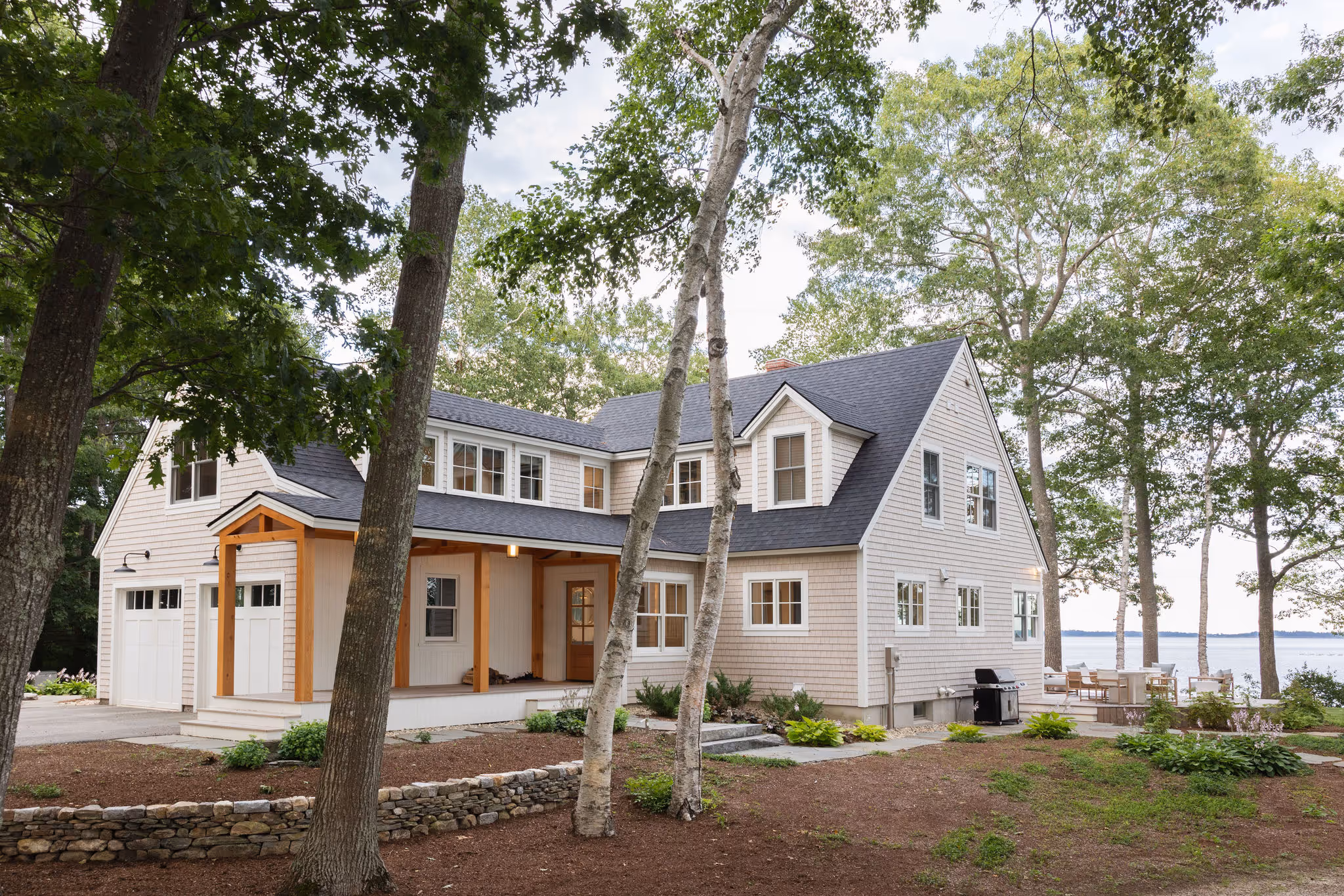 Coastal home with white siding, wooden porch, surrounded by trees near water
