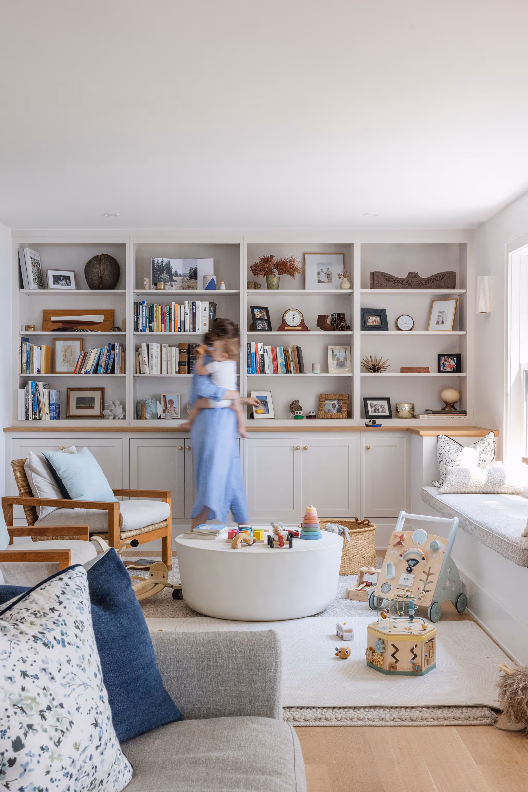 Cozy living room with built-in bookshelves, toys, and blurred figure of a person