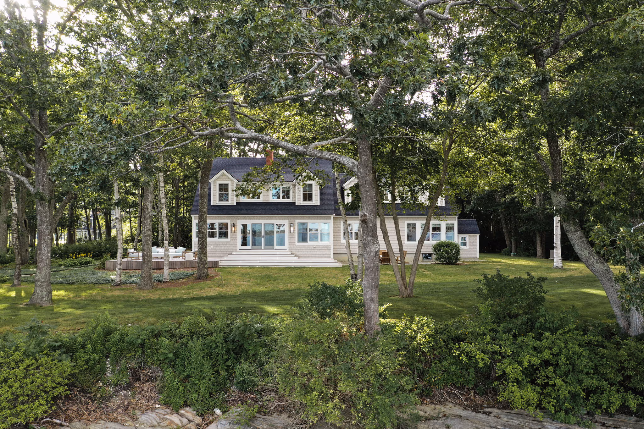 Coastal home nestled among trees with spacious lawn and wooden deck