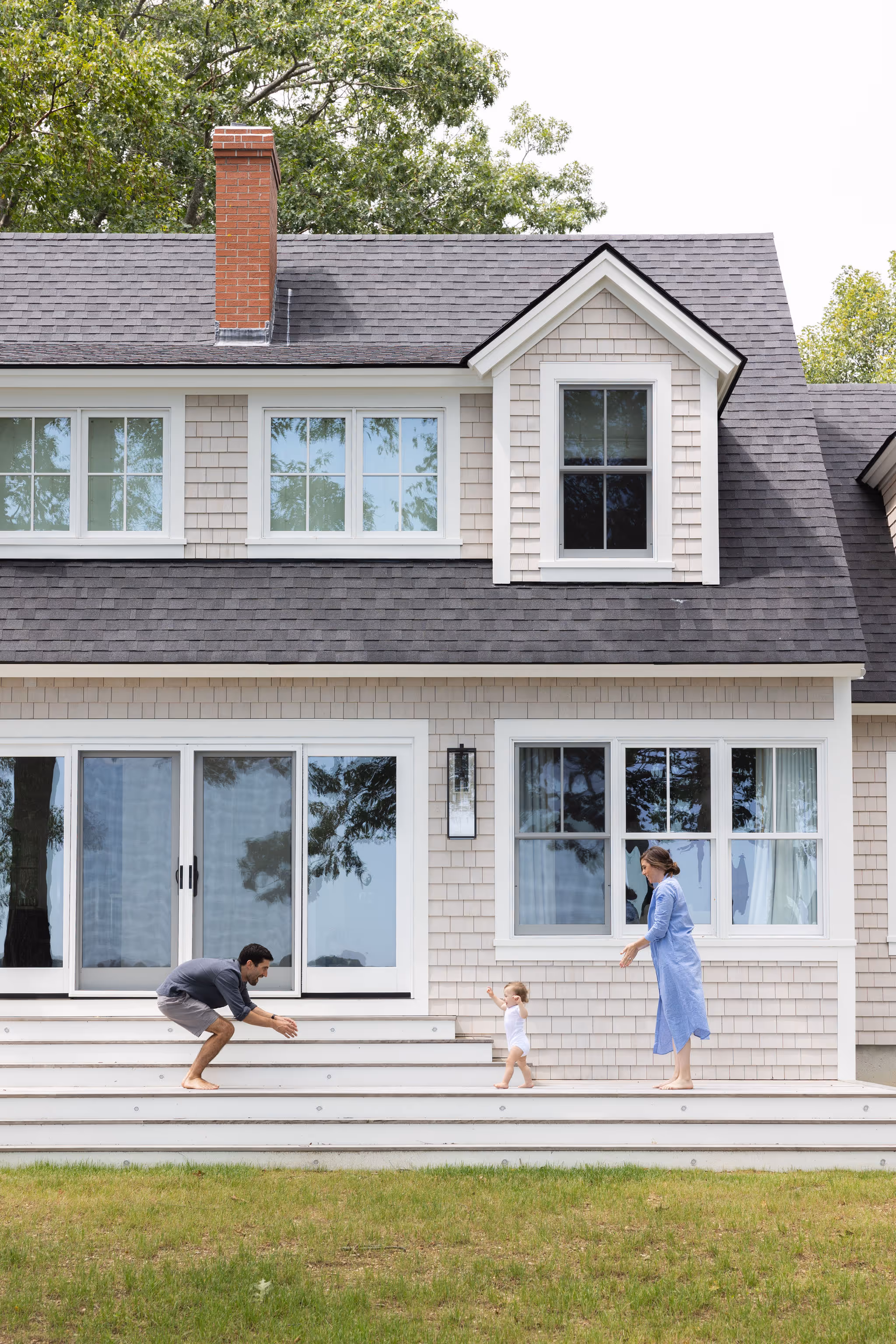 Parent and child playing on porch of shingle-style coastal home
