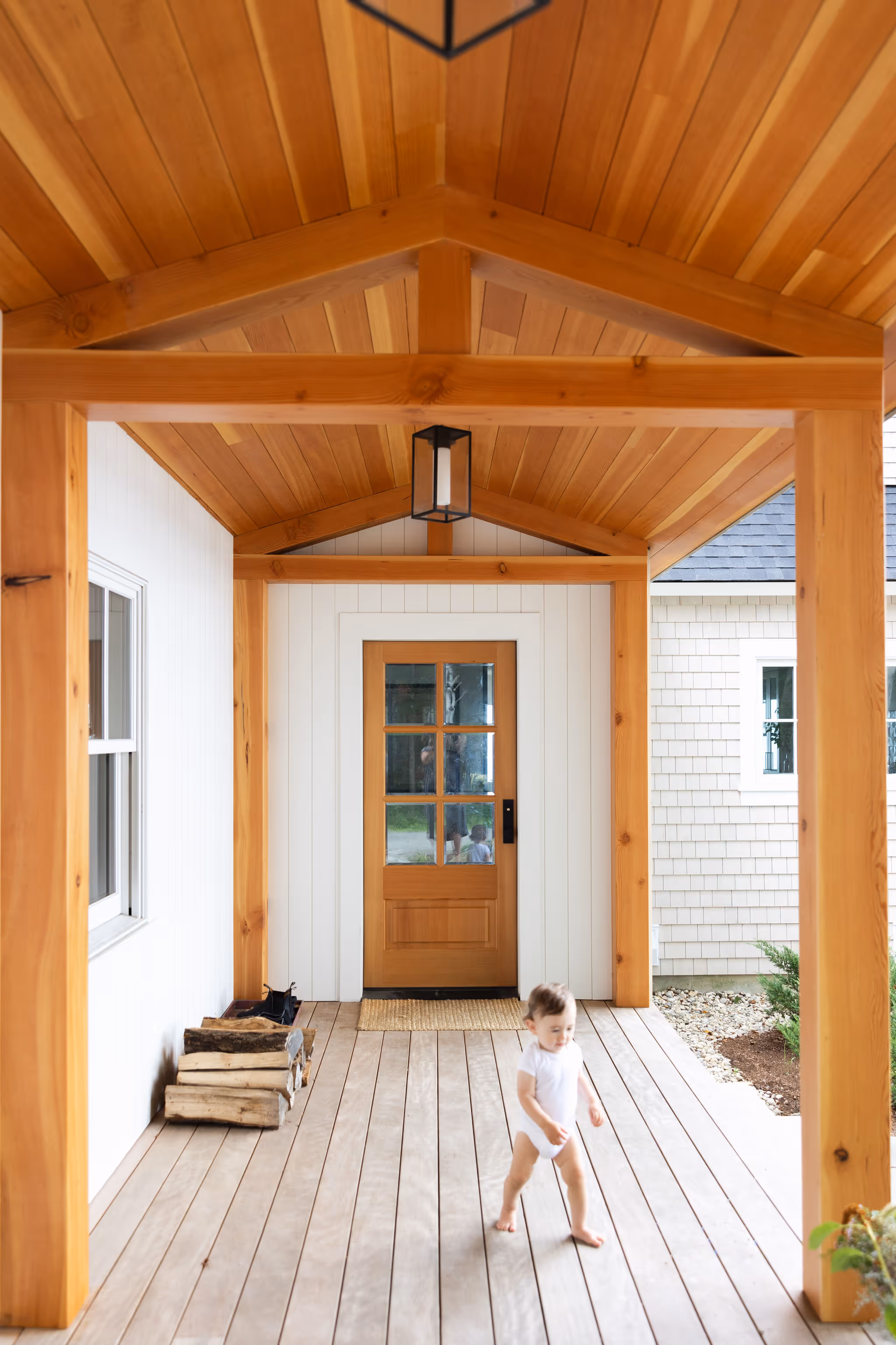 Wooden porch with white walls, glass door, and a child walking