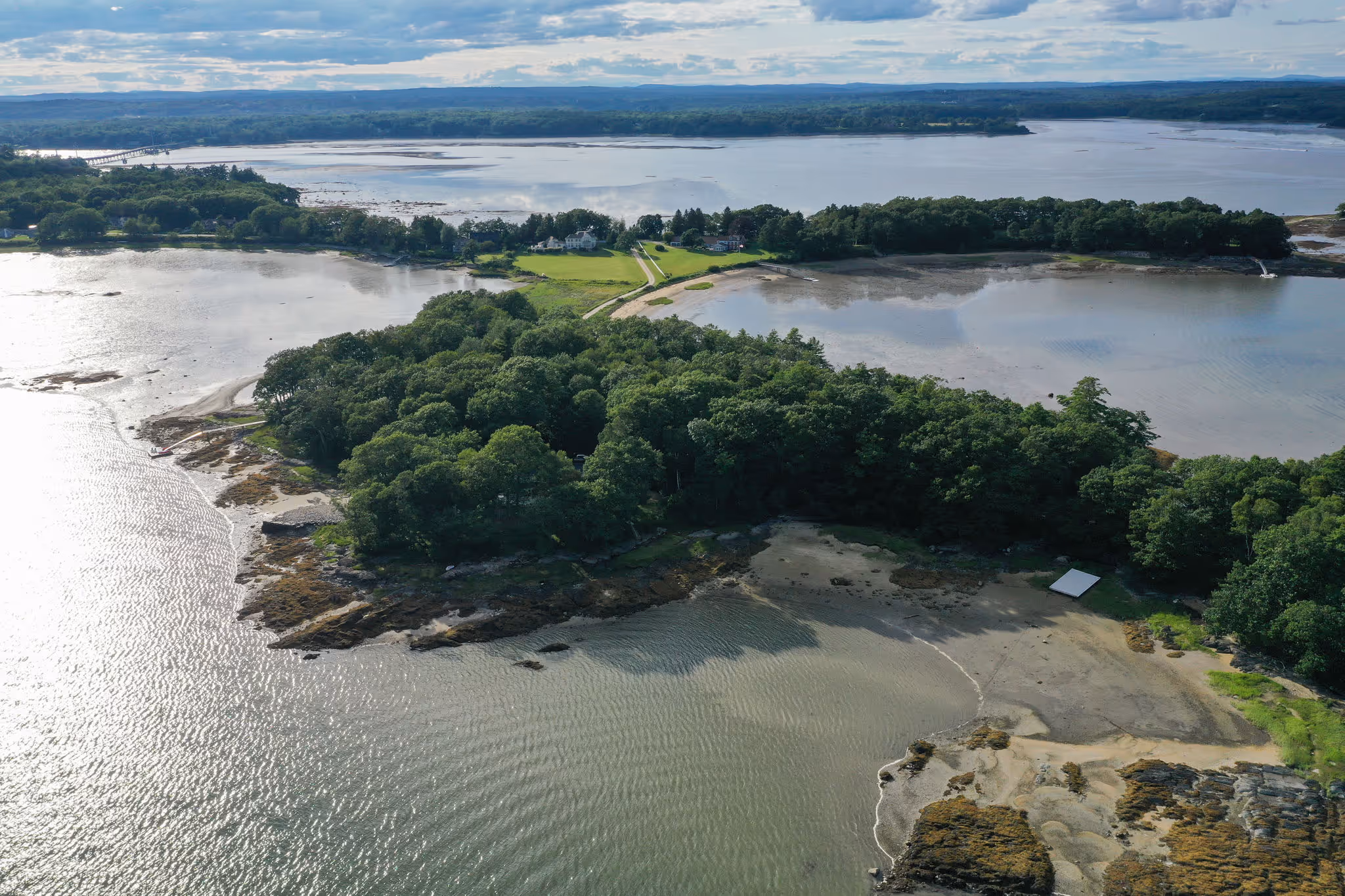 Aerial view of wooded coastal peninsula surrounded by calm water and rocky shoreline