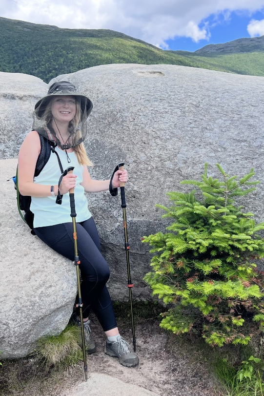 Person sitting between boulders holding hiking poles