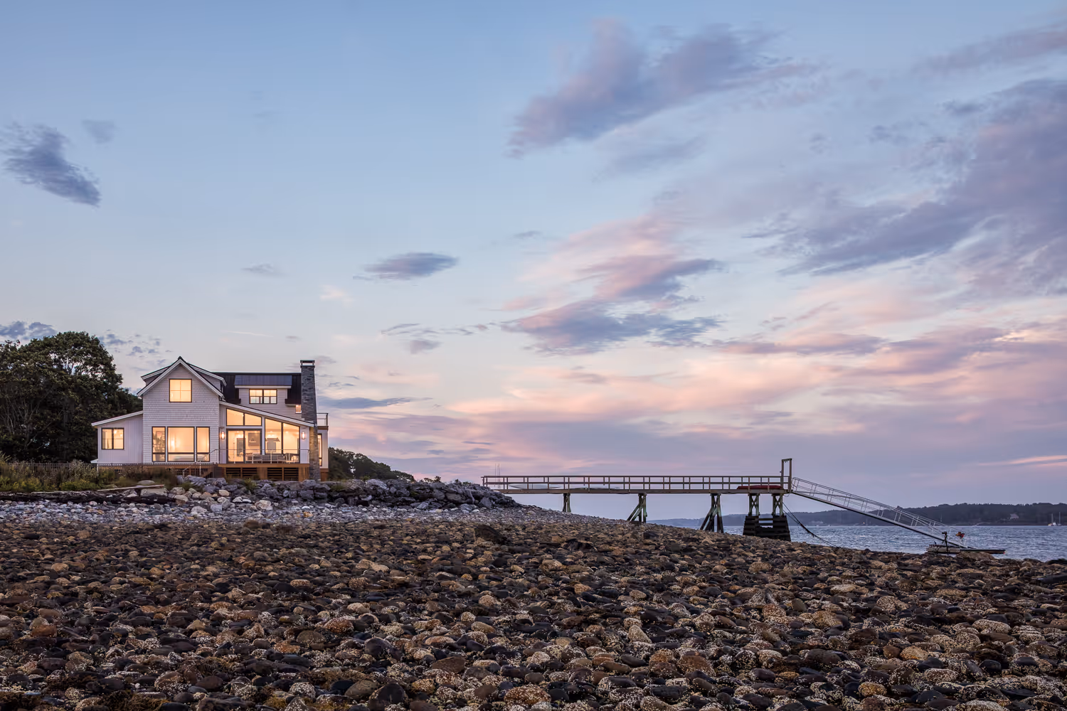 Cozy beach house with warm windows on rocky shore at twilight