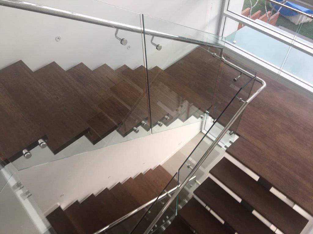 Glass stair balustrade with a stainless steel handrail on timber stairs