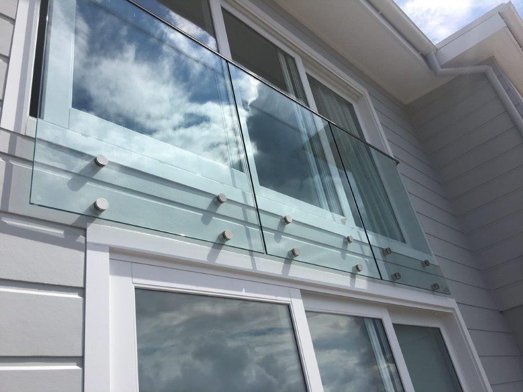 Staircase with tactile paving, metal handrails, and a lit handrail on a modern building, overlooking landscaped garden beds.