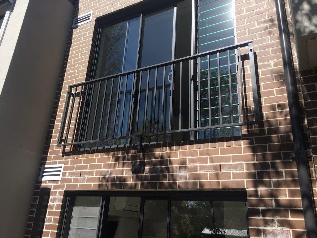 Brick building facade with metal balcony railing and large glass sliding doors.