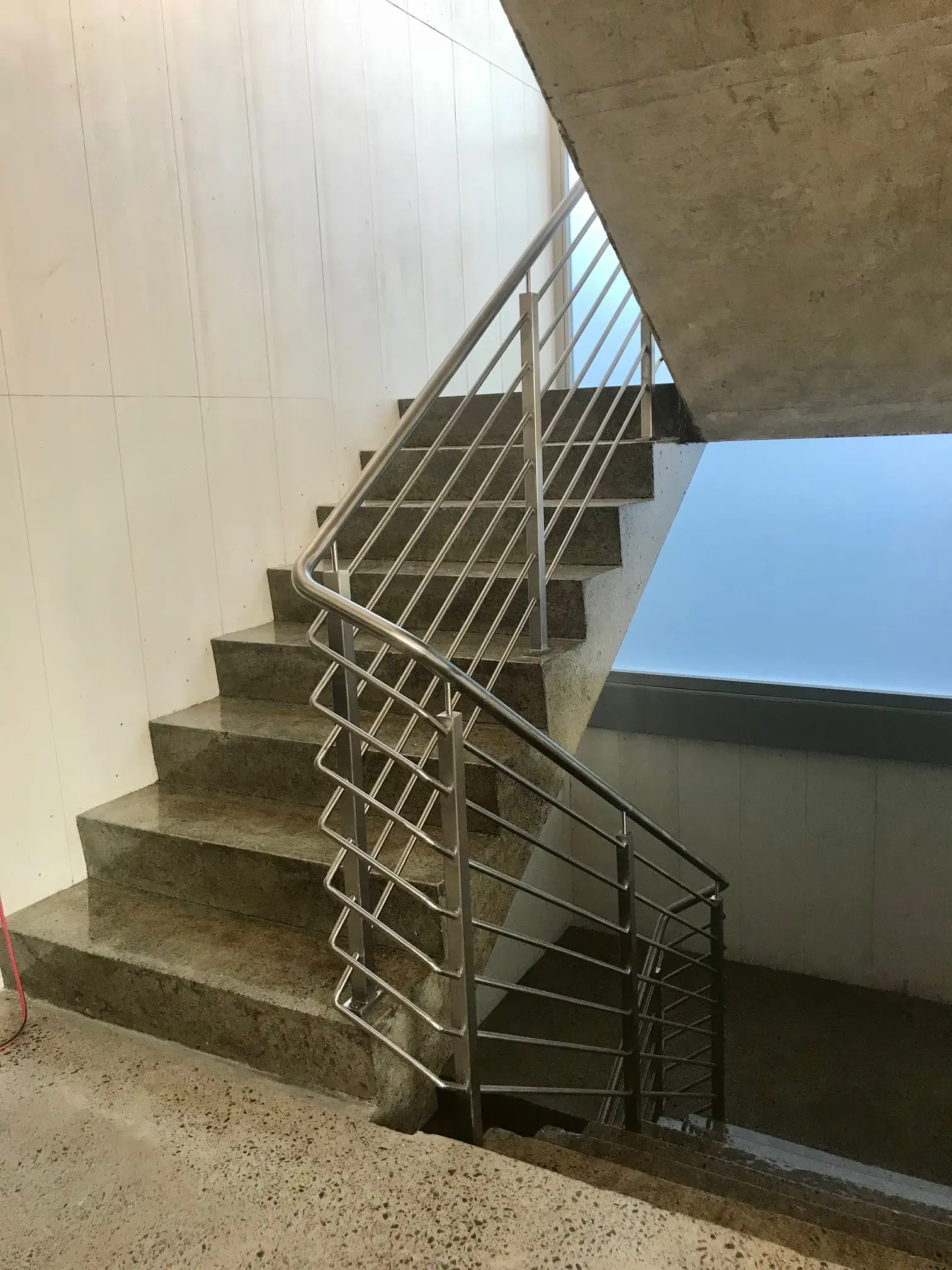 Concrete staircase with metal handrails inside a building with white walls and a large window.