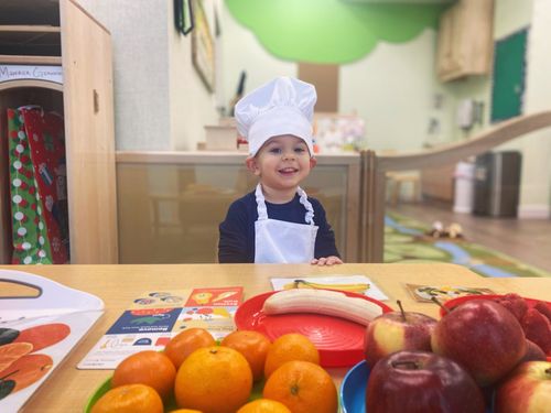 Child sitting in front of fruits, wearing a chef's hat