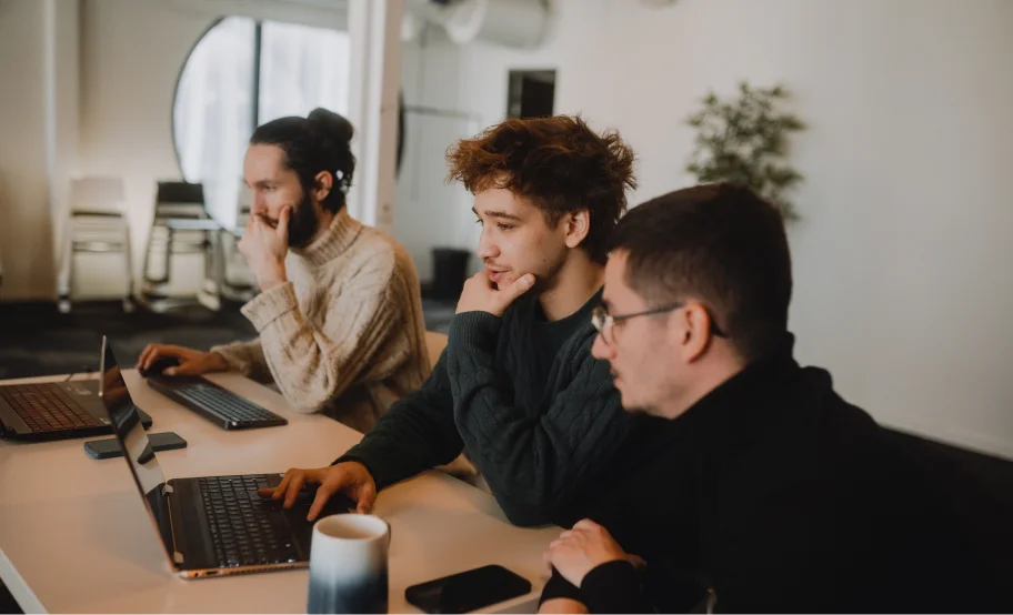 Three people sitting at a table using laptops, focusing on their screens.