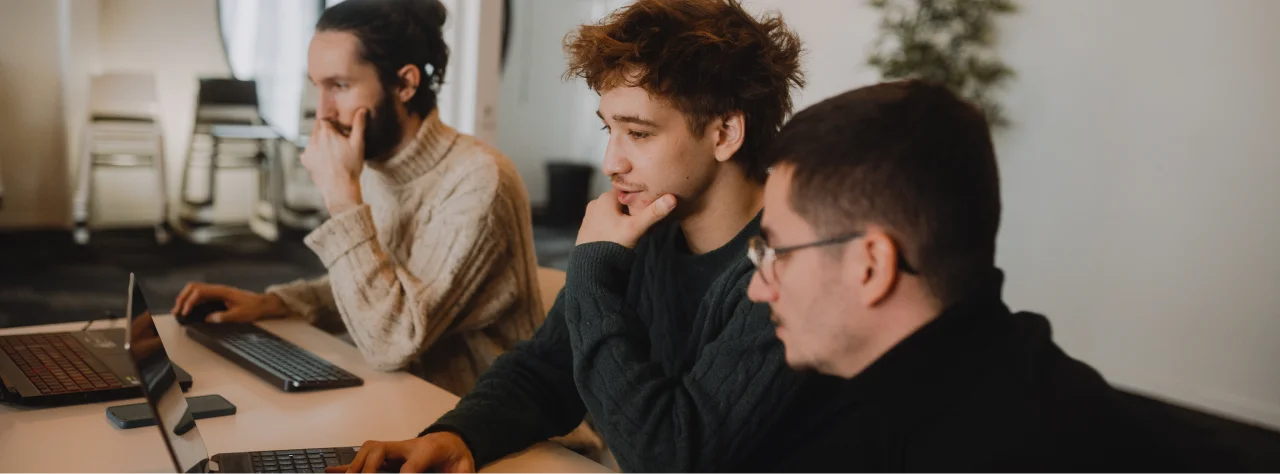 Trois hommes concentrés travaillant sur des ordinateurs portables dans un bureau.