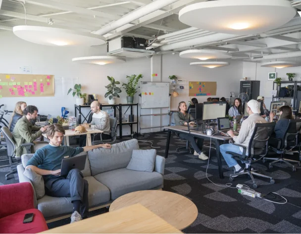 Bureau moderne avec plusieurs personnes travaillant sur des ordinateurs, entourés de plantes et de notes collantes sur les murs.