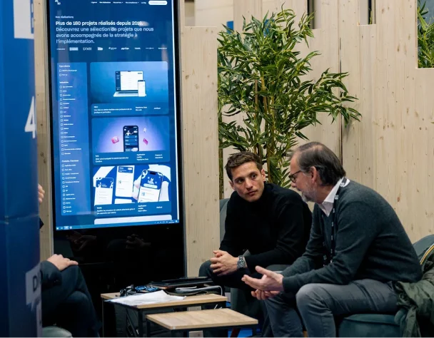 Two men sitting in chairs, having a conversation in front of a large digital screen.