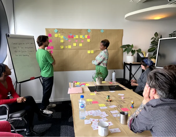 A person with glasses and a beard smiles while wearing a plaid shirt indoors.