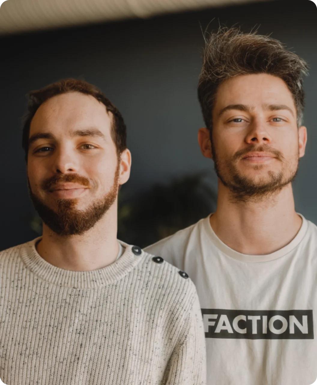 Two people standing close together, both looking at the camera and smiling slightly.