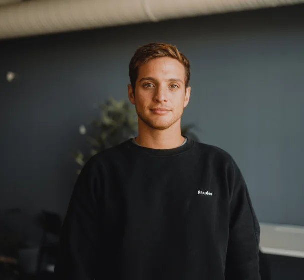 A smiling person with short hair wearing a black turtleneck looking at the camera.