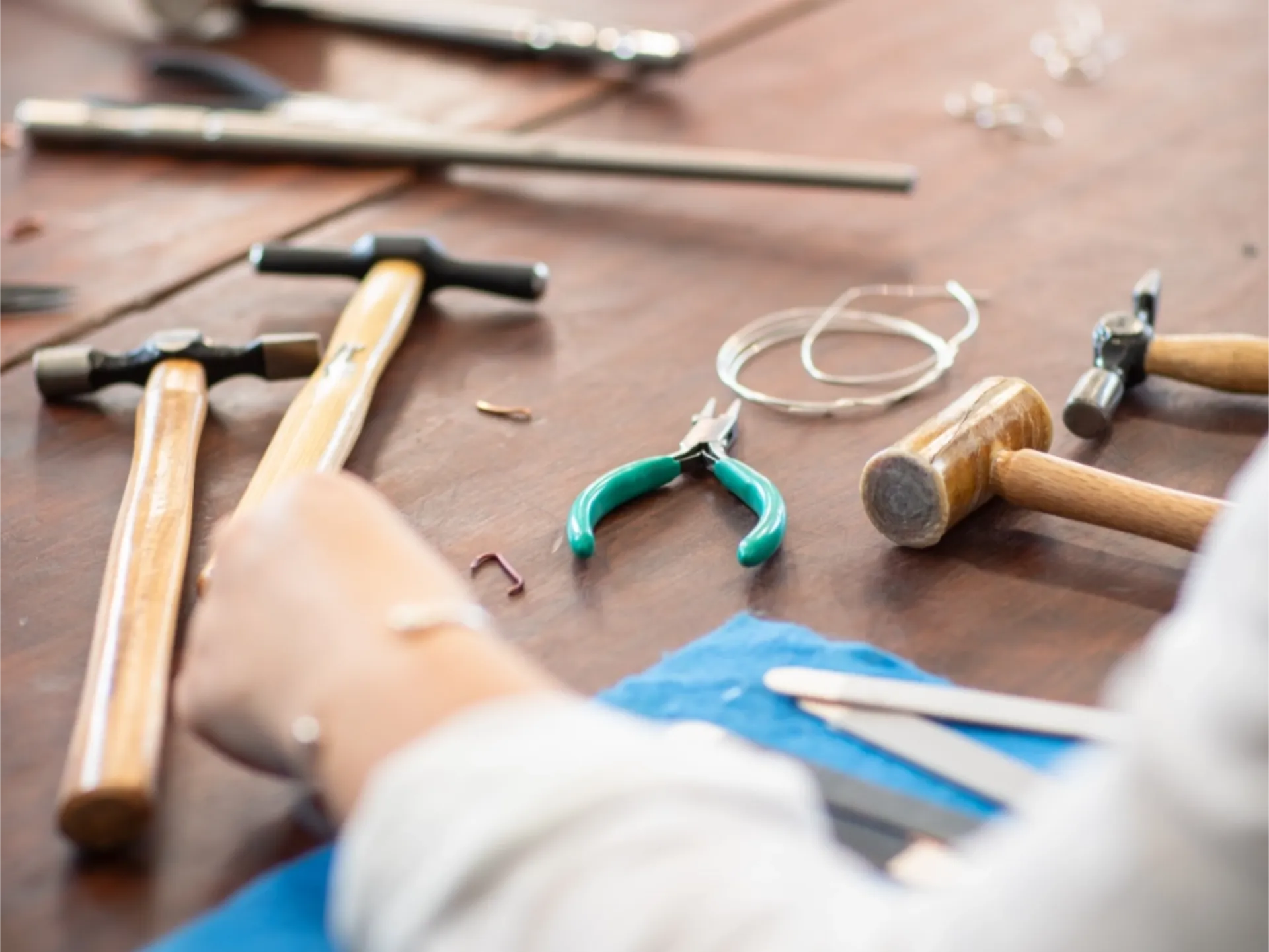 Wooden table with assorted small hammers, pliers, metal wire, and a person working with tools.