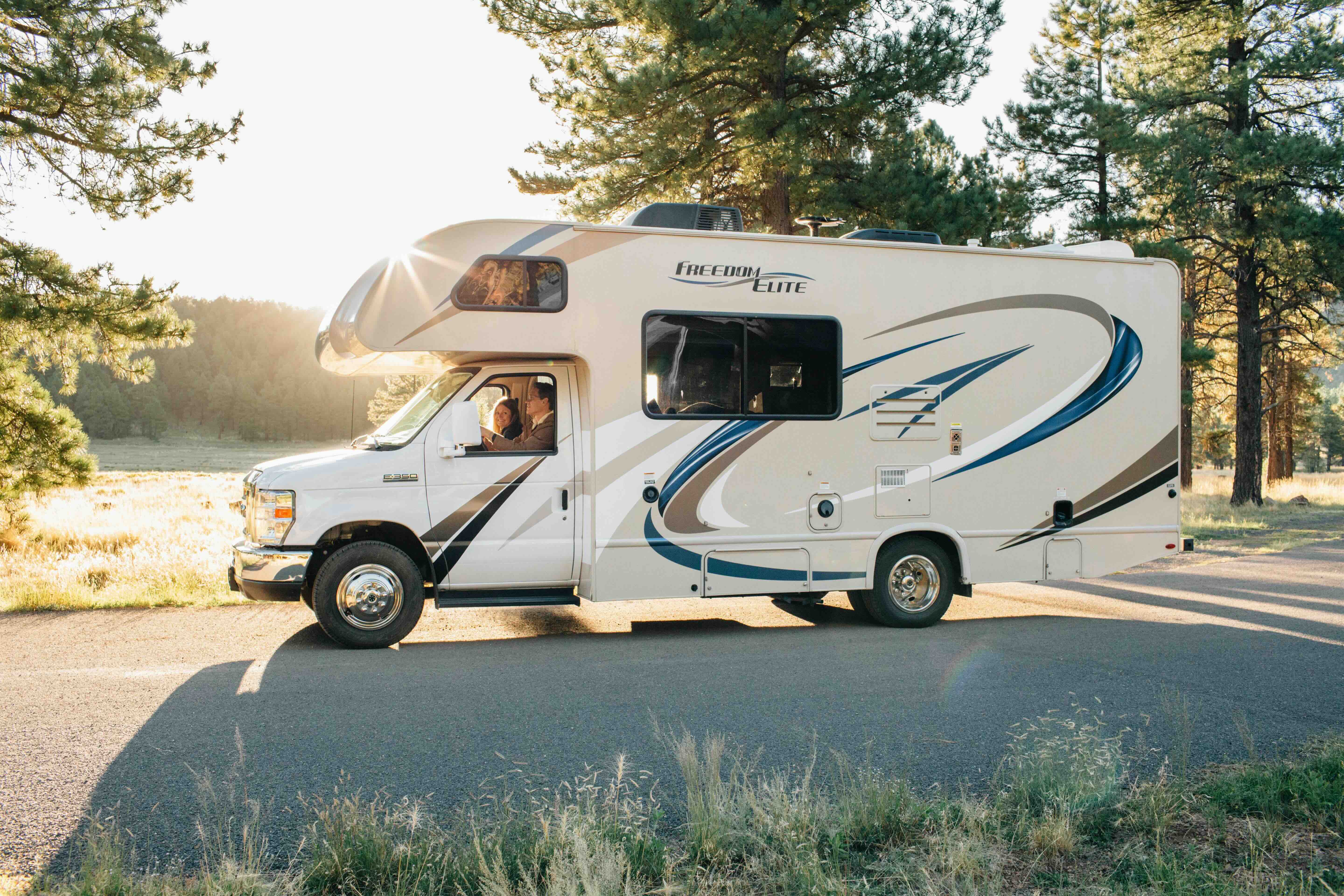 An RV driving down a tree lined road at sunset