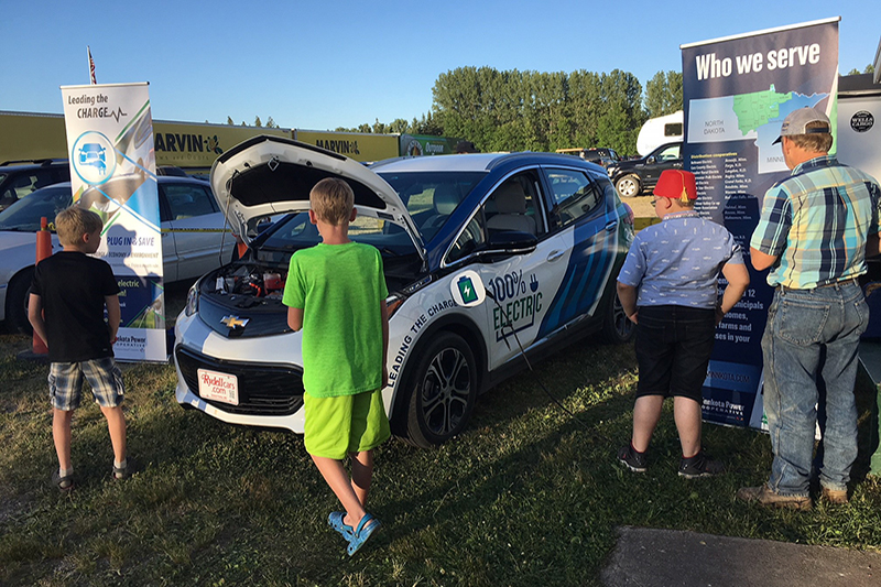 A few people looking at Minnkota's Bolt electric vehicle on a nice day at the Roseau County Fair.