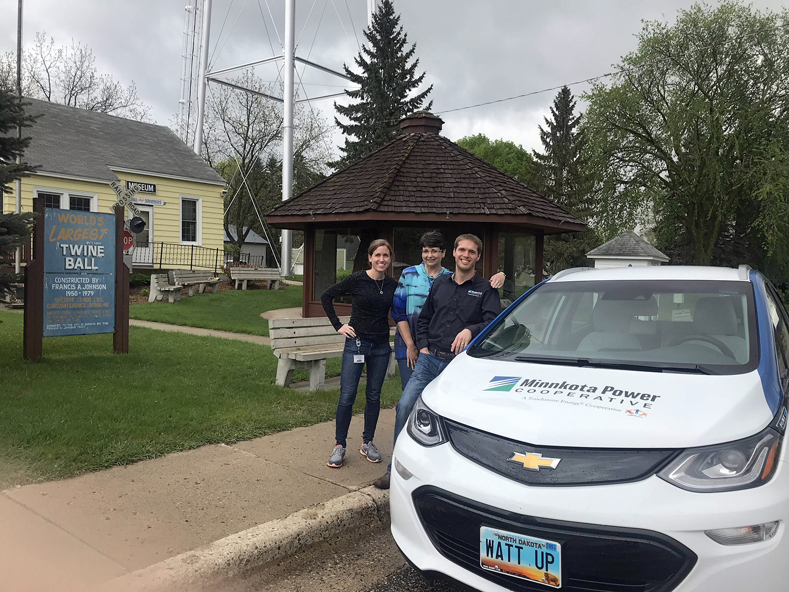 A few employees from Minnkota standing by the Bolt electric vehicle near a sign for the world's largest twine ball.
