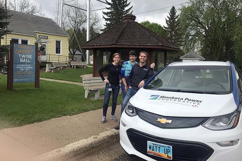 A few employees from Minnkota standing by the Bolt electric vehicle near a sign for the world's largest twine ball.