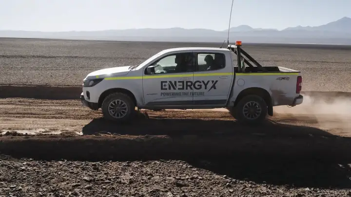 A white pickup truck with "ENERGYX POWERING THE FUTURE" logo drives on a dirt road in a desert.