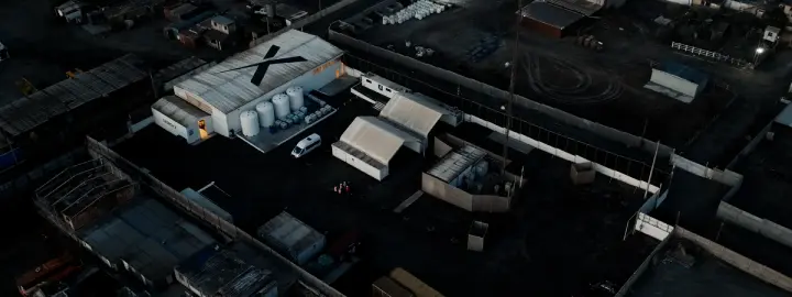 Aerial view of an industrial site with multiple buildings, including one with a large "X" on its roof, at dusk.